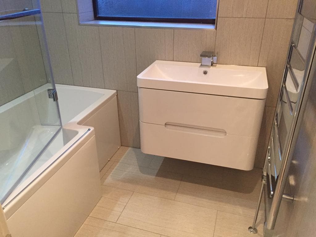 Wall-hung vanity unit beside a shower bath with glass screen